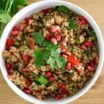 Bulgur and mung bean salad in a white bowl on a wooden table with fresh parsley on the side.