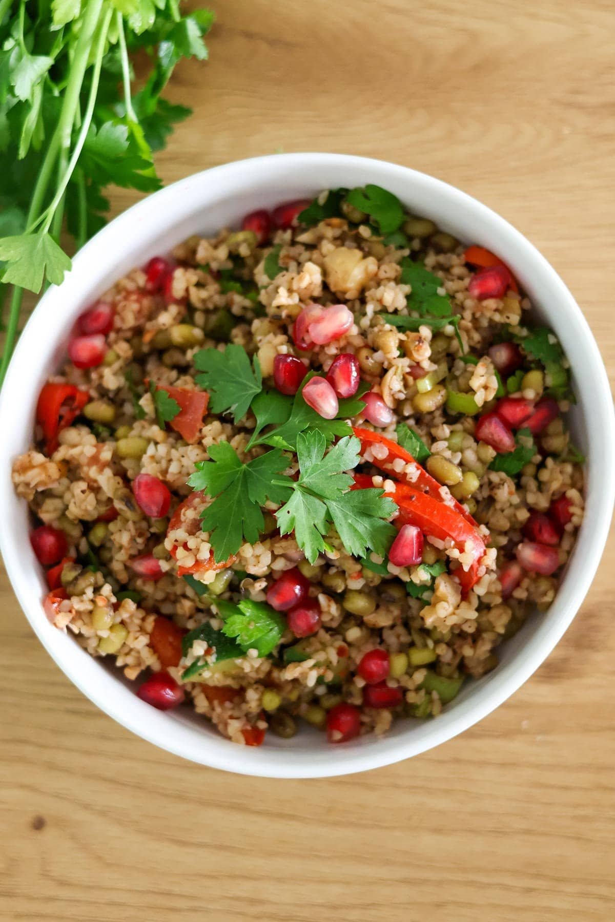 Bulgur and mung bean salad in a white bowl on a wooden table with fresh parsley on the side.