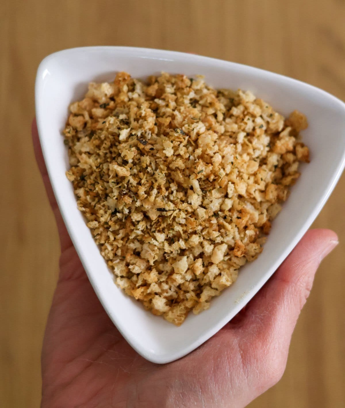 A hand holds a with bowl with breadcrumbs.