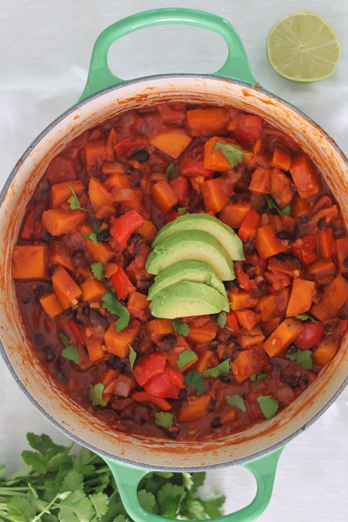 Chili in a green pot topped with avocado and fresh cilantro.