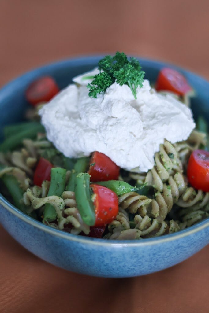 Vegan pasta pesto with cherry tomatoes, green beans, vegan ricotta cheese and fresh parsley on top.