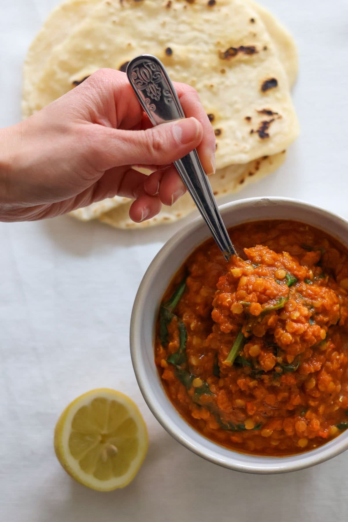 A hand holds a silver spoon in the masoor dal.