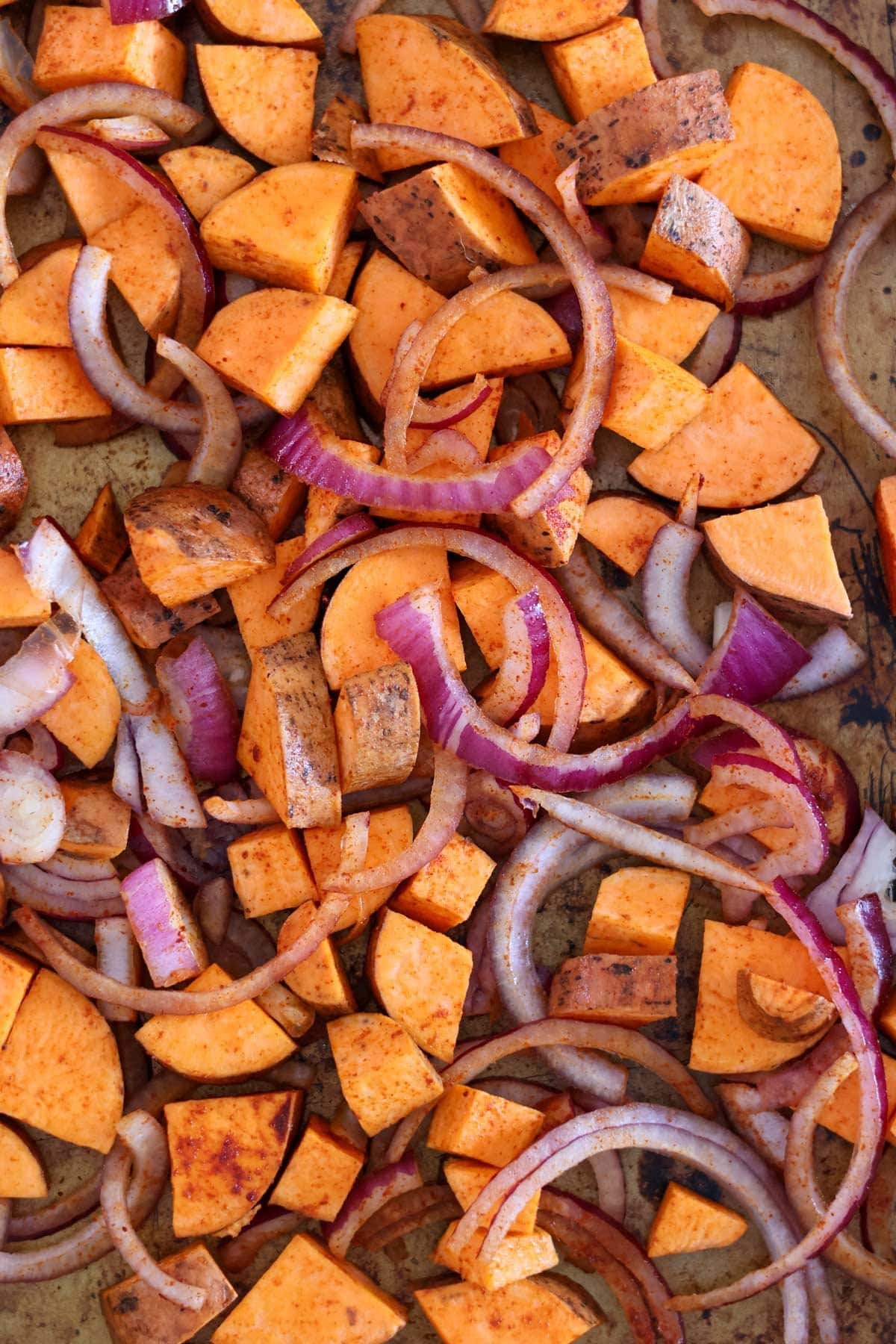 pieces of sweet potato and red onion on a baking sheet.