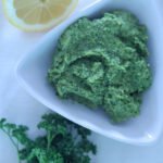 Fresh parsley, half a lemon and a white bowl of vegan green pesto.