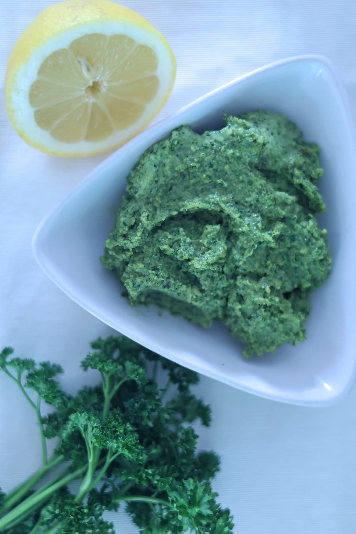 Fresh parsley, half a lemon and a white bowl of vegan green pesto.