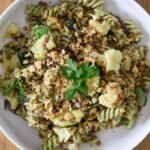 Vegan pasta salad with cauliflower, zucchini and red onion in a white bowl on a wooden table.