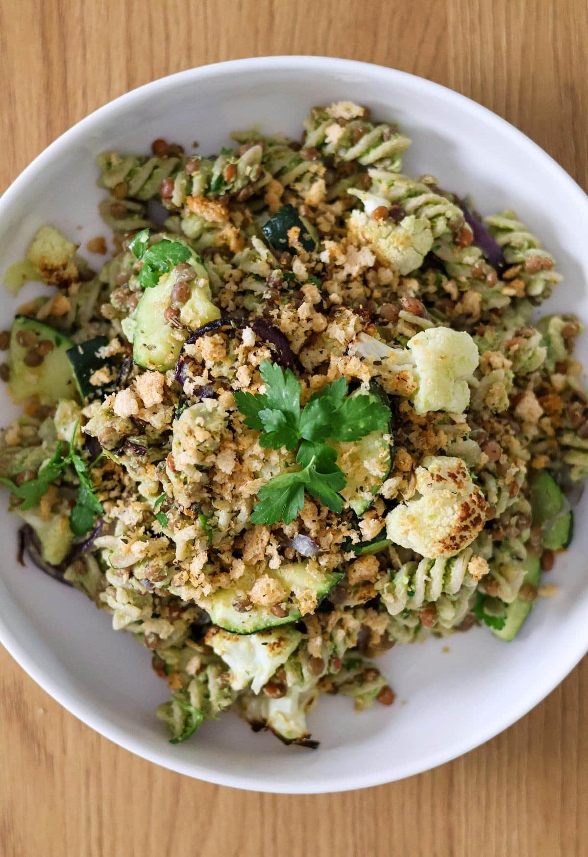 Vegan pasta salad with cauliflower, zucchini and red onion in a white bowl on a wooden table.