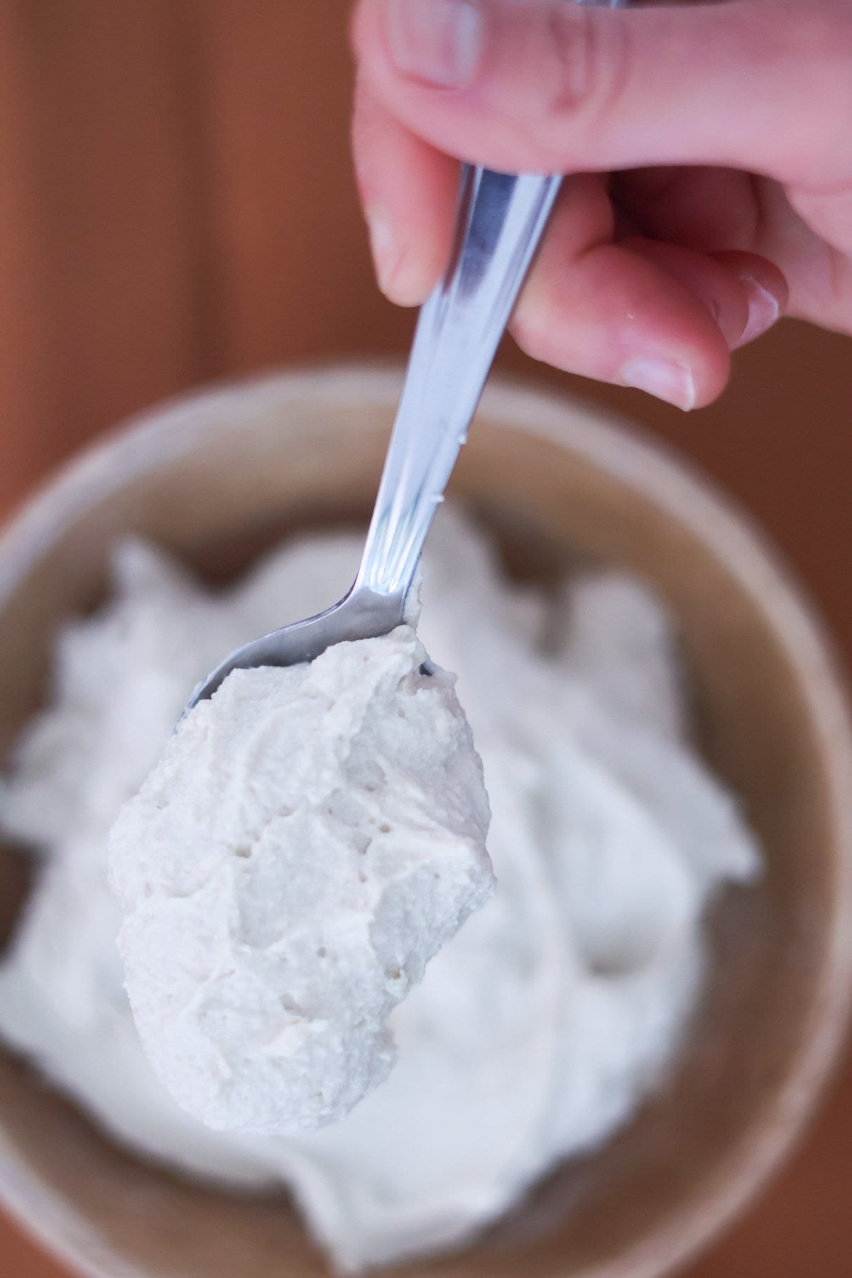A hand holds a silver spoon with vegan ricotta cheese.