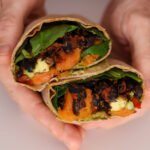 Two hands holding a wrap cut in half filled with black beans, spinach and sweet potato.