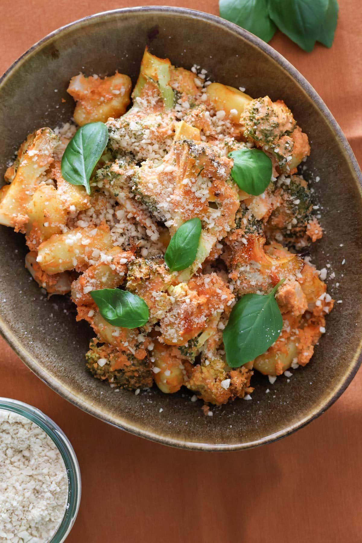 Easy Oven-Baked Vegan Gnocchi in a brown bowl topped with fresh basil and vegan parmesan cheese.