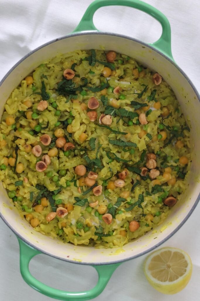 Orzo with chickpeas, peas, lemon, fennel, fresh mint and roasted hazelnuts in a green pan.