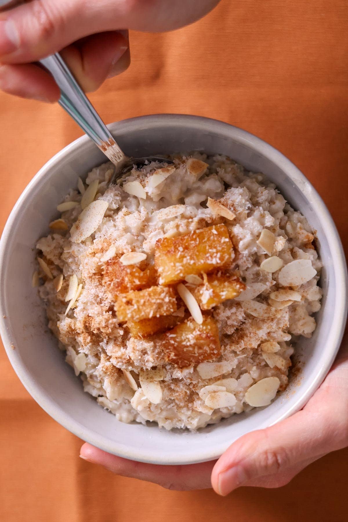 Oatmeal with coconut milk and pineapple in a white bowl with a silver spoon.