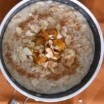 Oatmeal in a green saucepan topped with pineapple, cinnamon, shredded coconut and slivered toasted almonds.