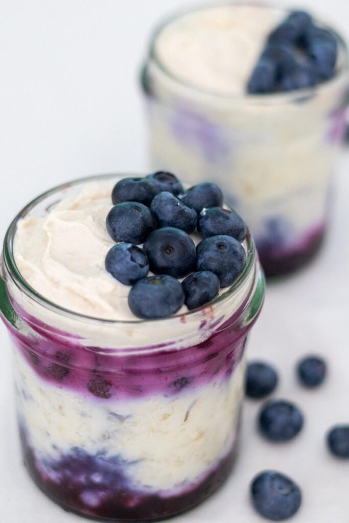 Two small mason jars filled with blueberry cheesecake overnight oats with fresh blueberries on top and on the side.