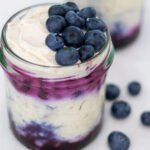 Two small mason jars filled with blueberry cheesecake overnight oats with fresh blueberries on top and on the side.