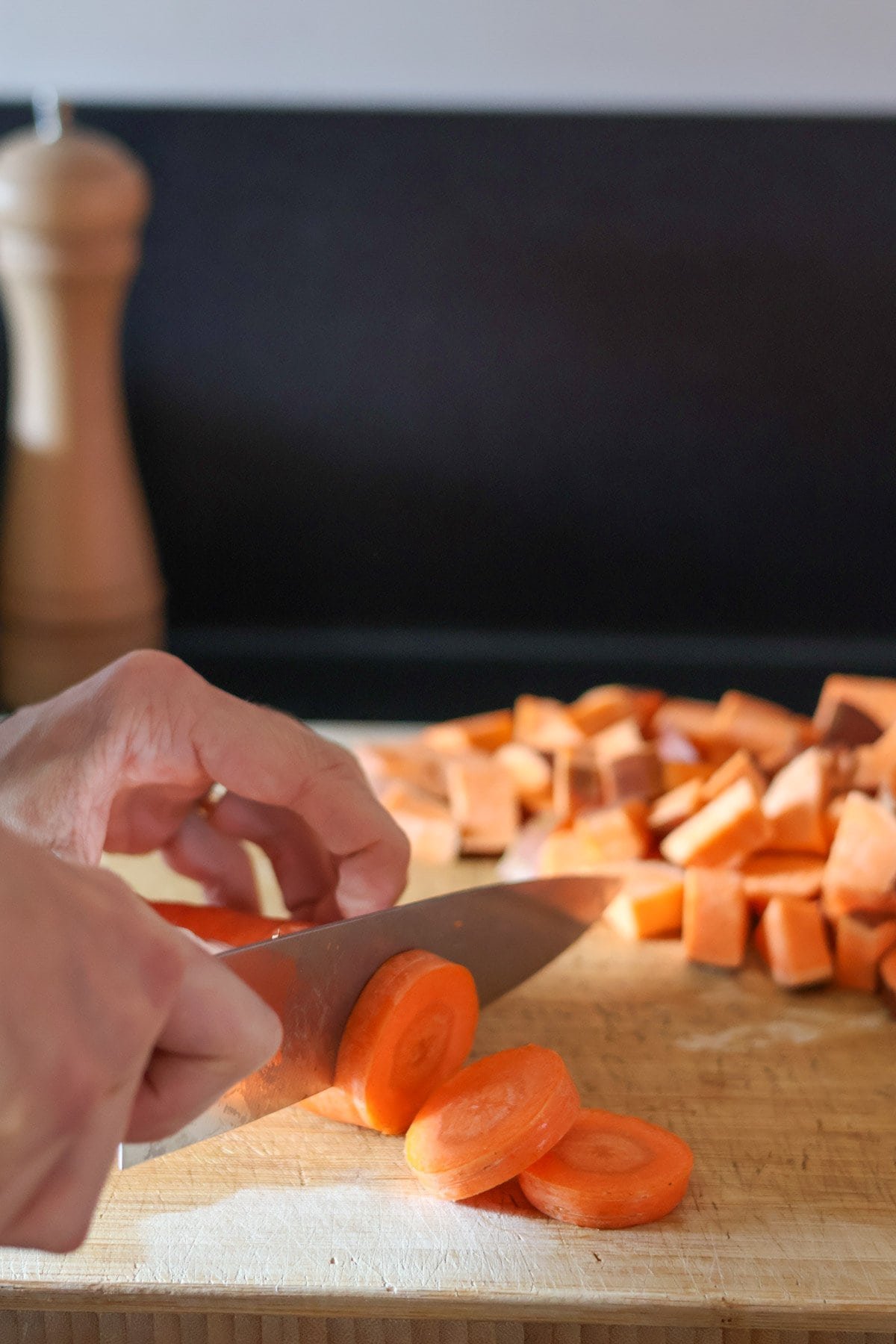 A carrot is cut into slices with a silver knife on a wooden cutting board.