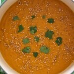 Carrot Sweet Potato and Ginger Soup in a large green pot topped with sesame seeds and fresh cilantro.