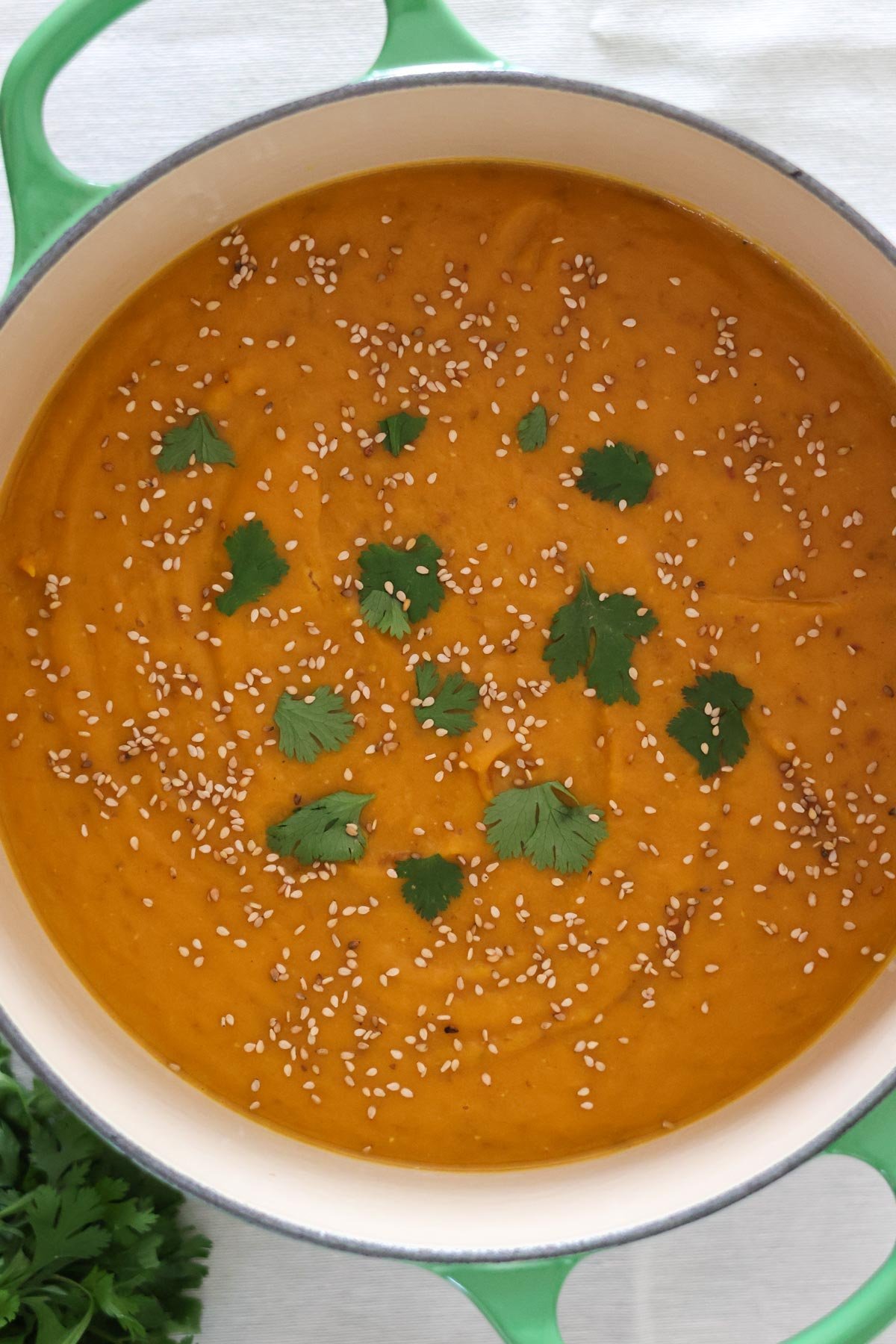 Carrot Sweet Potato and Ginger Soup in a large green pot topped with sesame seeds and fresh cilantro.