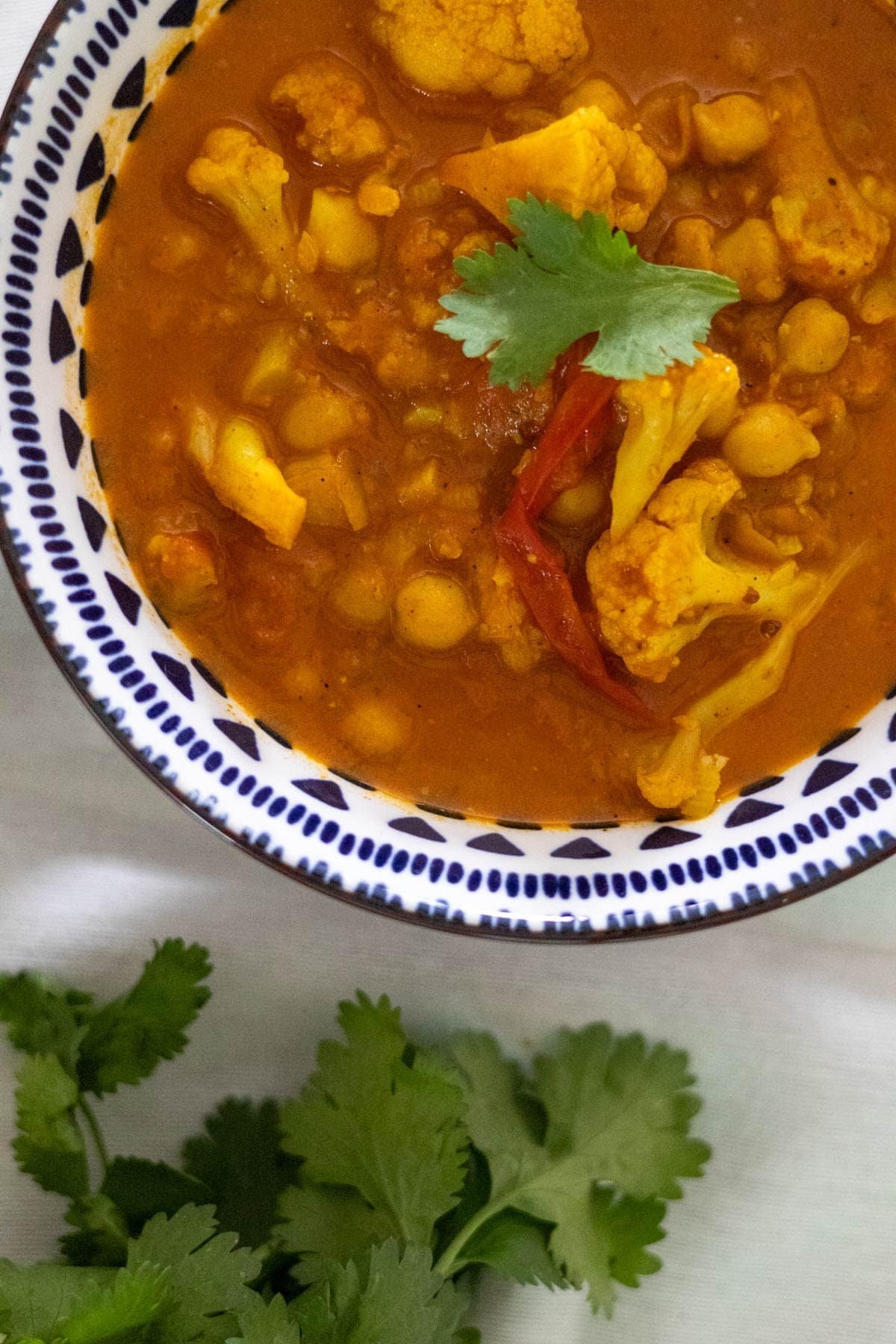 Cauliflower and chickpea curry in a blue and white bowl with fresh cilantro on top and on the side.