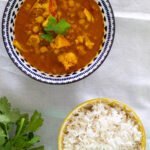 Cauliflower and chickpea curry in a white and blue bowl with fresh cilantro and rice in another bowl on the side.