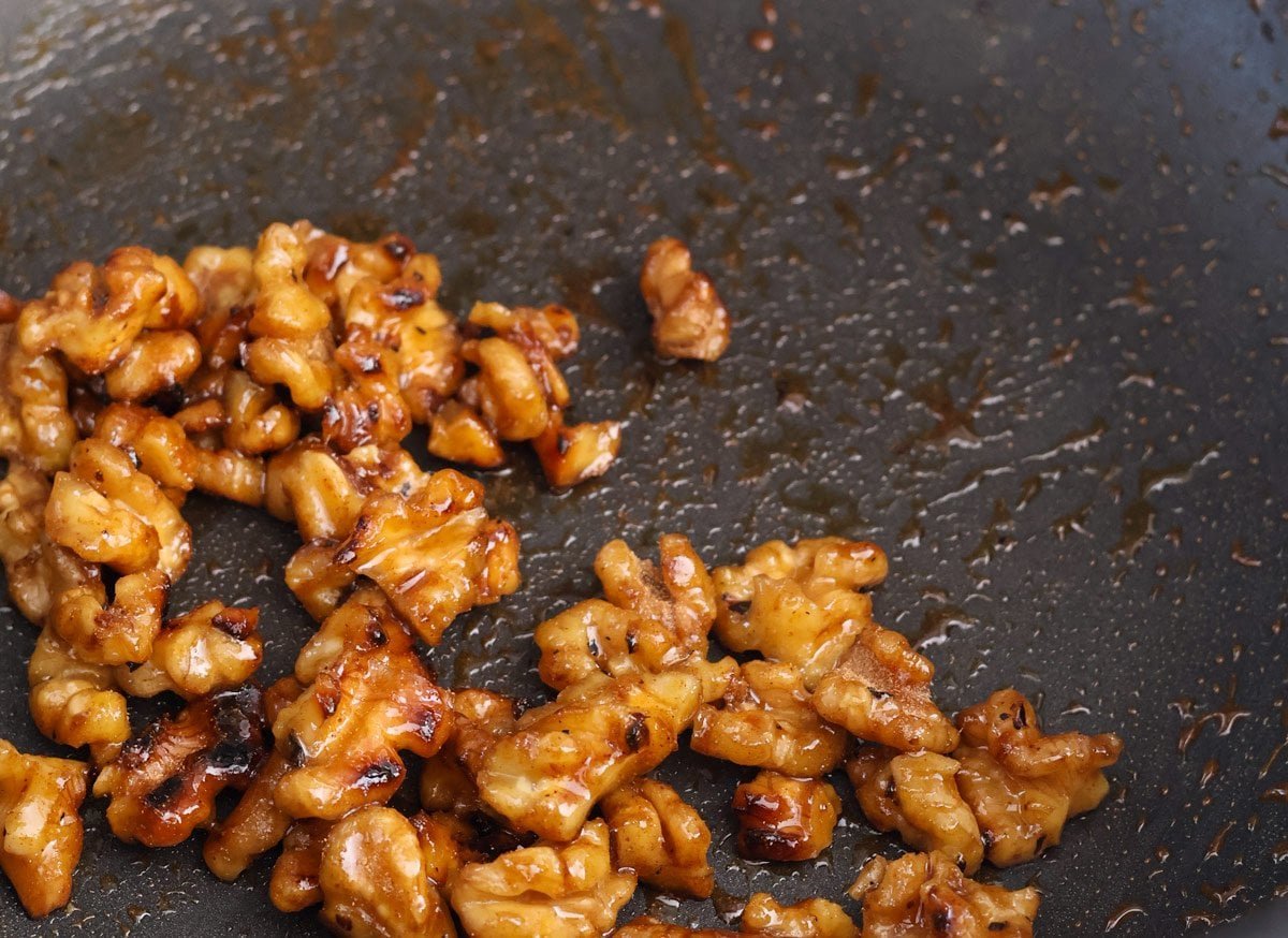 Caramelized sticky walnuts in a black skillet.