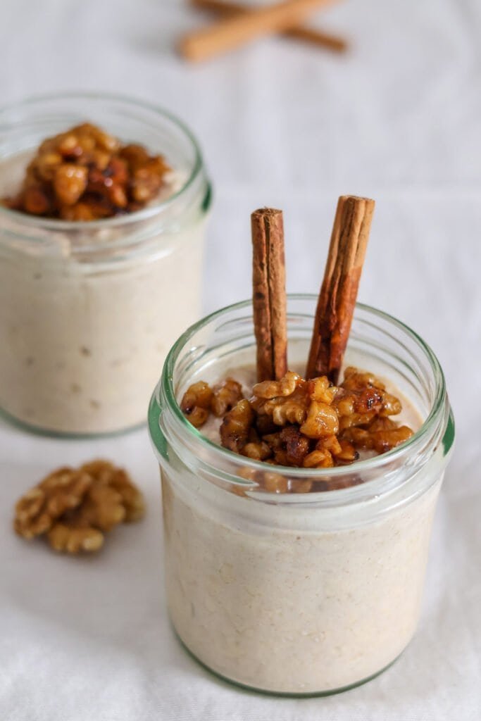 Two jars filled with cinnamon roll overnight oats, sticky walnuts and cinnamon sticks.
