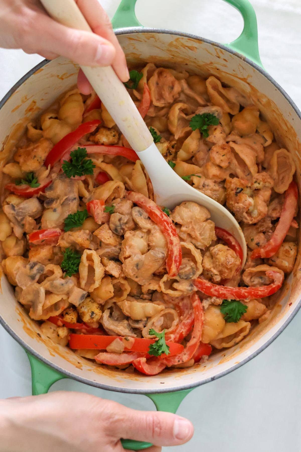 The Healthy Vegan Mushroom Stroganoff with pasta and parsley is scooped up with a spoon from a large green pot.