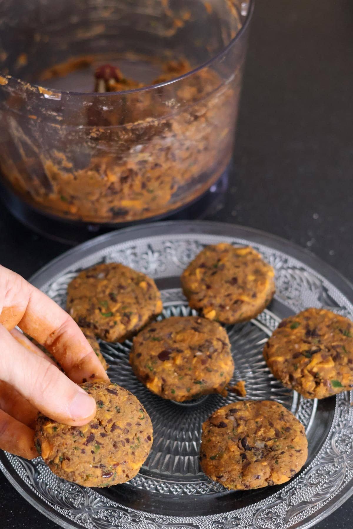 A hand places a raw vegan sweet potato cake on a plate with more raw vegan sweet potato cakes.