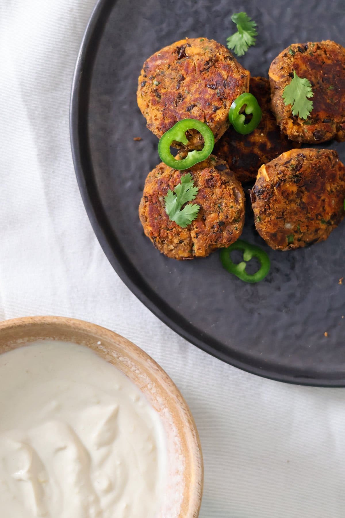 Healthy vegan sweet potato cakes on a black plate with a lemon tahini yogurt sauce on the side. 