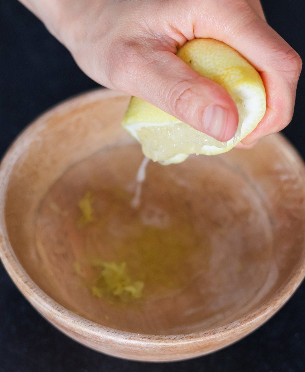 A hand squeezes juice from half a lemon into a wooden bowl.