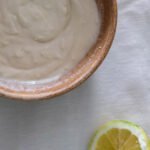 Lemon Tahini Yogurt Sauce in a wooden bowl with half a lemon on the side.