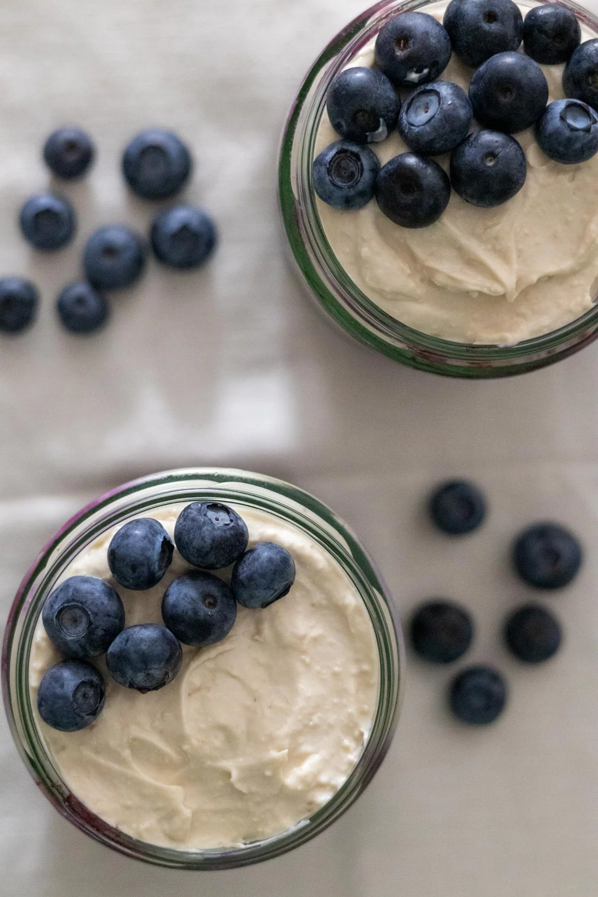 Two small mason jars filled with blueberry cheesecake overnight oats with fresh blueberries on top and on the side.