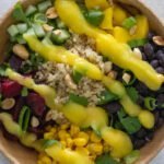 Cooked quinoa, diced cucumber, black beans, corn, cubed beets and cubed mango in a wooden bowl topped with mango sauce, peanuts, spring onion and cilantro.