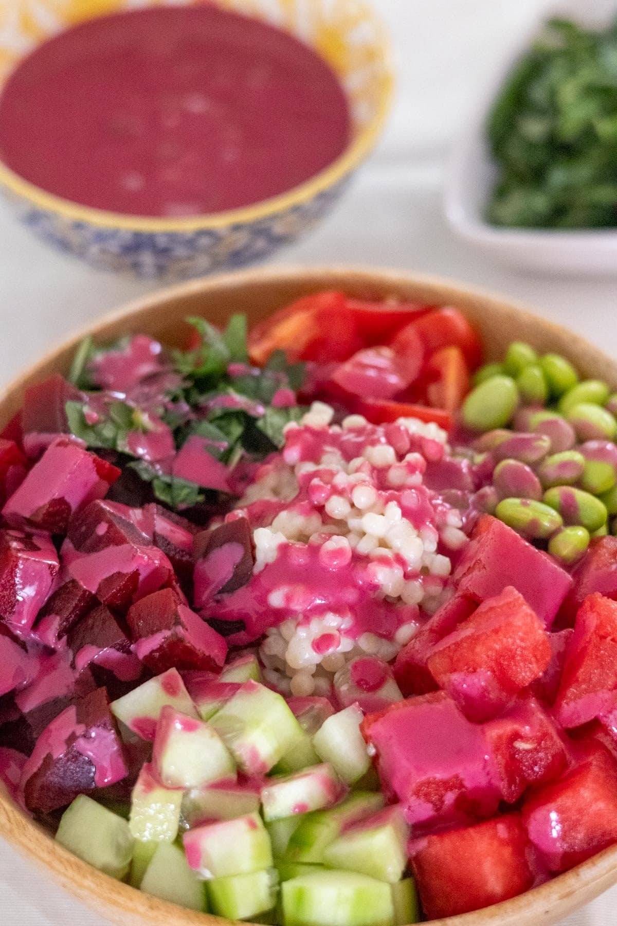 Watermelon, beetroot, cucumber, cherry tomatoes, edamame, pearl couscous, fresh mint and Thai Basil in a wooden bowl served with a beetroot sauce.