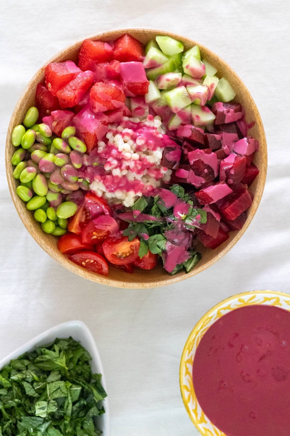 Watermelon, beetroot, cucumber, cherry tomatoes, edamame, pearl couscous, fresh mint and Thai Basil in a wooden bowl served with a beetroot sauce.