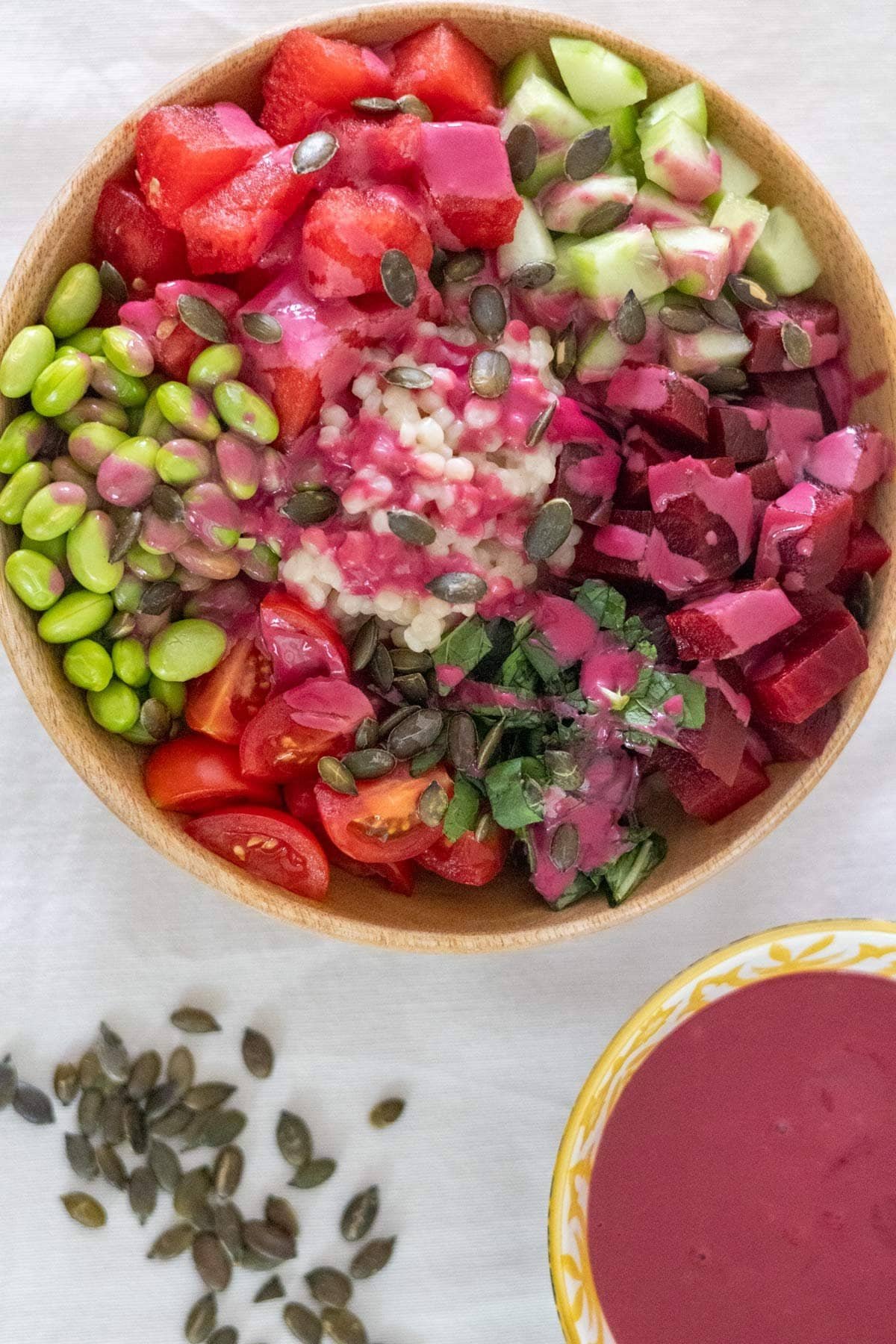 Watermelon, beetroot, cucumber, cherry tomatoes, edamame, pearl couscous, fresh mint and Thai Basil in a wooden bowl served with a beetroot sauce and pumpkin seeds.