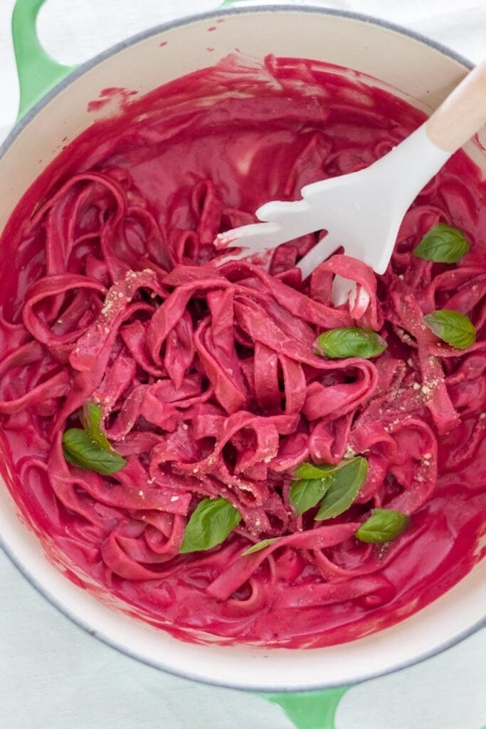 Tagliatelle with a beetroot pasta sauce in a large pot topped with fresh basil and vegan parmesan cheese.