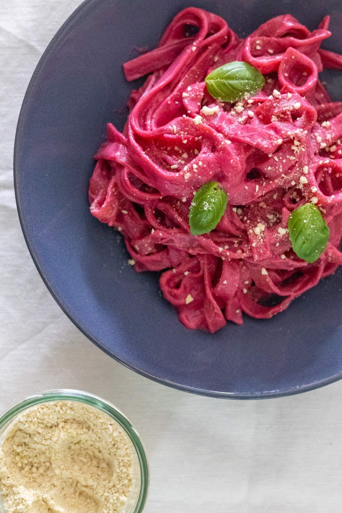 Tagliatelle covered in a beetroot pasta sauce topped with fresh basil and vegan parmesan cheese with extra vegan parmesan cheese on the side.