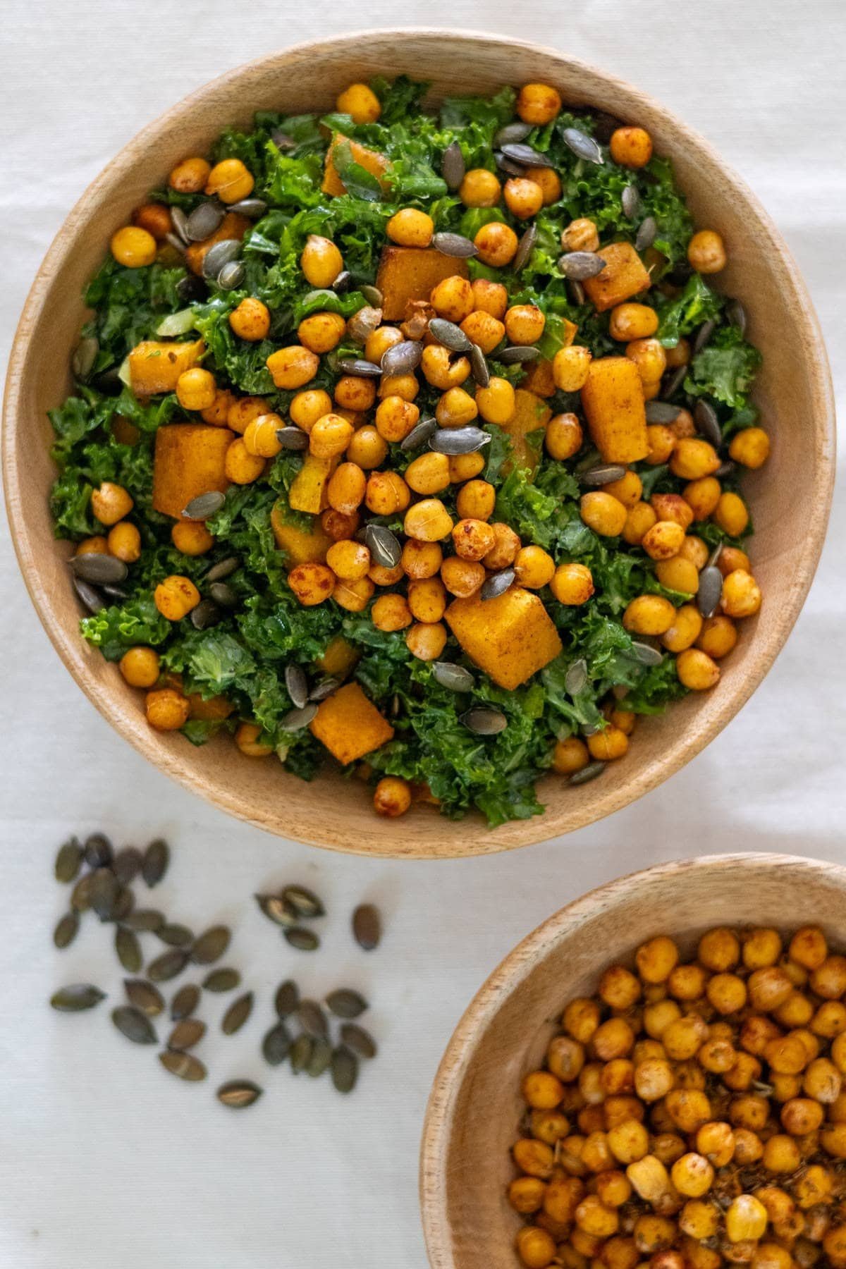 Kale, pumpkin seeds, roasted pumpkin and chickpeas in a wooden bowl served with crunchy chickpeas on the side.