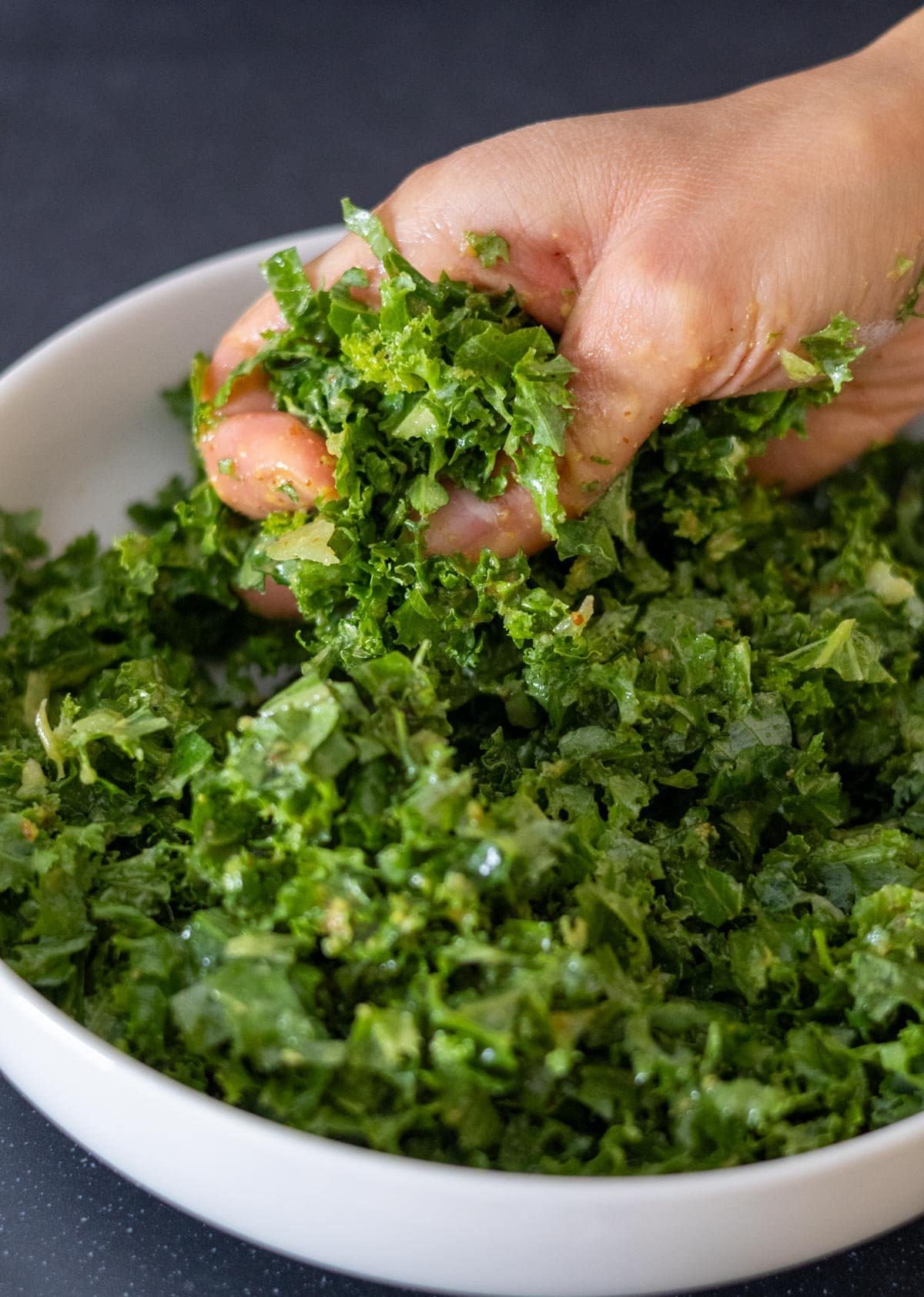 A hand massages the kale with the dressing