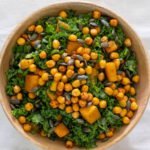 A wooden bowl filled with kale, pumpkin seeds, roasted pumpkin and crunchy chickpeas.