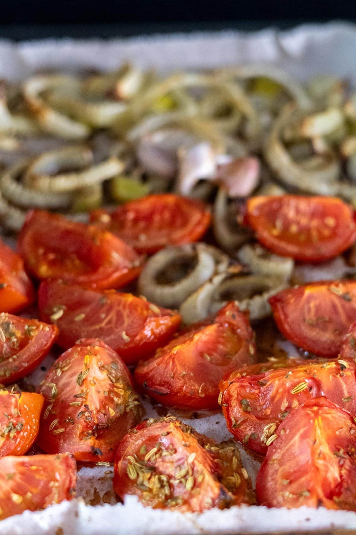 Roasted tomatoes, fennel and garlic on a baking tray topped with fennel seeds and oregano.