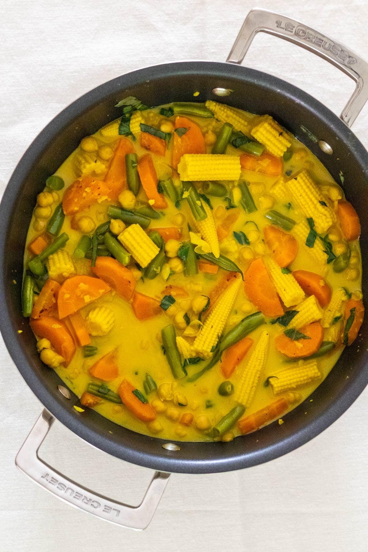 Vegan Thai Yellow Curry with green beans, carrot, baby corn and chickpeas in a black wok.