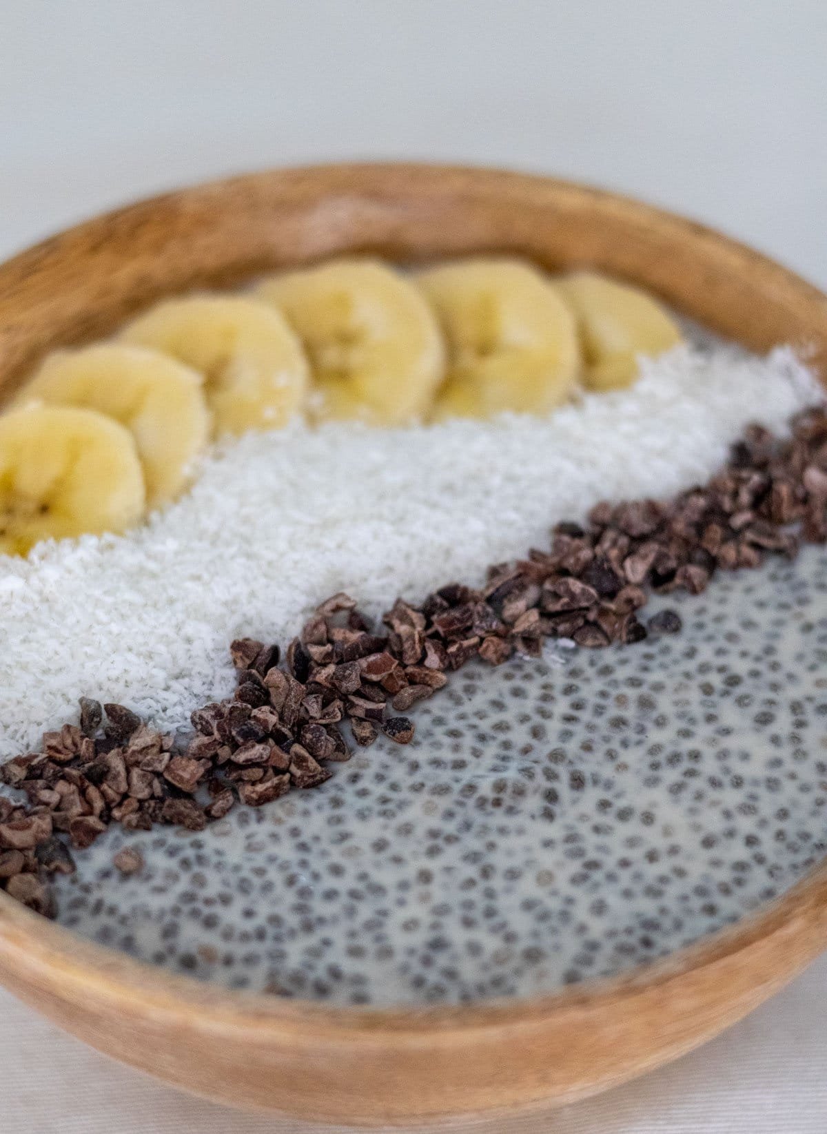 Coconut Chia Pudding in a wooden bowl topped with cocoa nibs, grated coconut and banana.