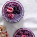 Two small mason jars filled with Berry Chia Pudding and topped with frozen raspberries and blueberries.