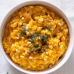 Pumpkin and Sage Risotto in a small white bowl topped with sage and pine nuts.