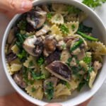 Cooked pasta with spinach, mushrooms and fresh parsley in a white bowl.