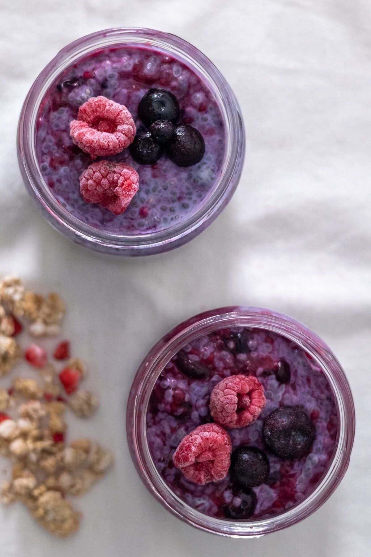 Two small mason jars filled with Berry Chia Pudding topped with frozen raspberries and blueberries.