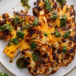 Two Vegan Cauliflower Steaks on a white plate topped with Chimichurri.